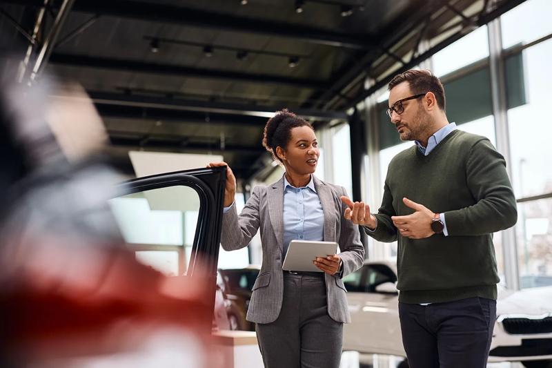 Mid adult man talking to African American saleswoman while buying new car in auto salon.