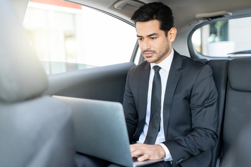 Hispanic young businessman using laptop while traveling in taxi