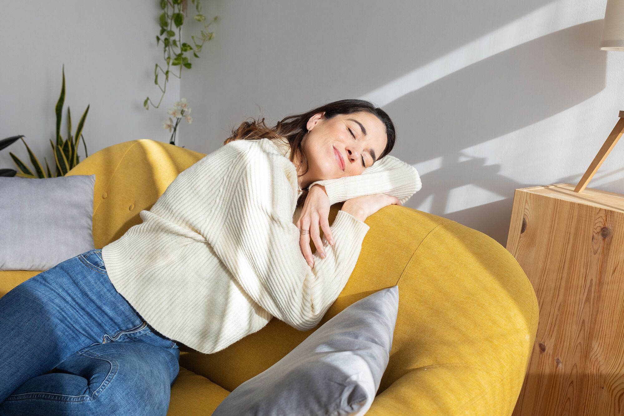 Woman enjoying sunlight resting on sofa at home.