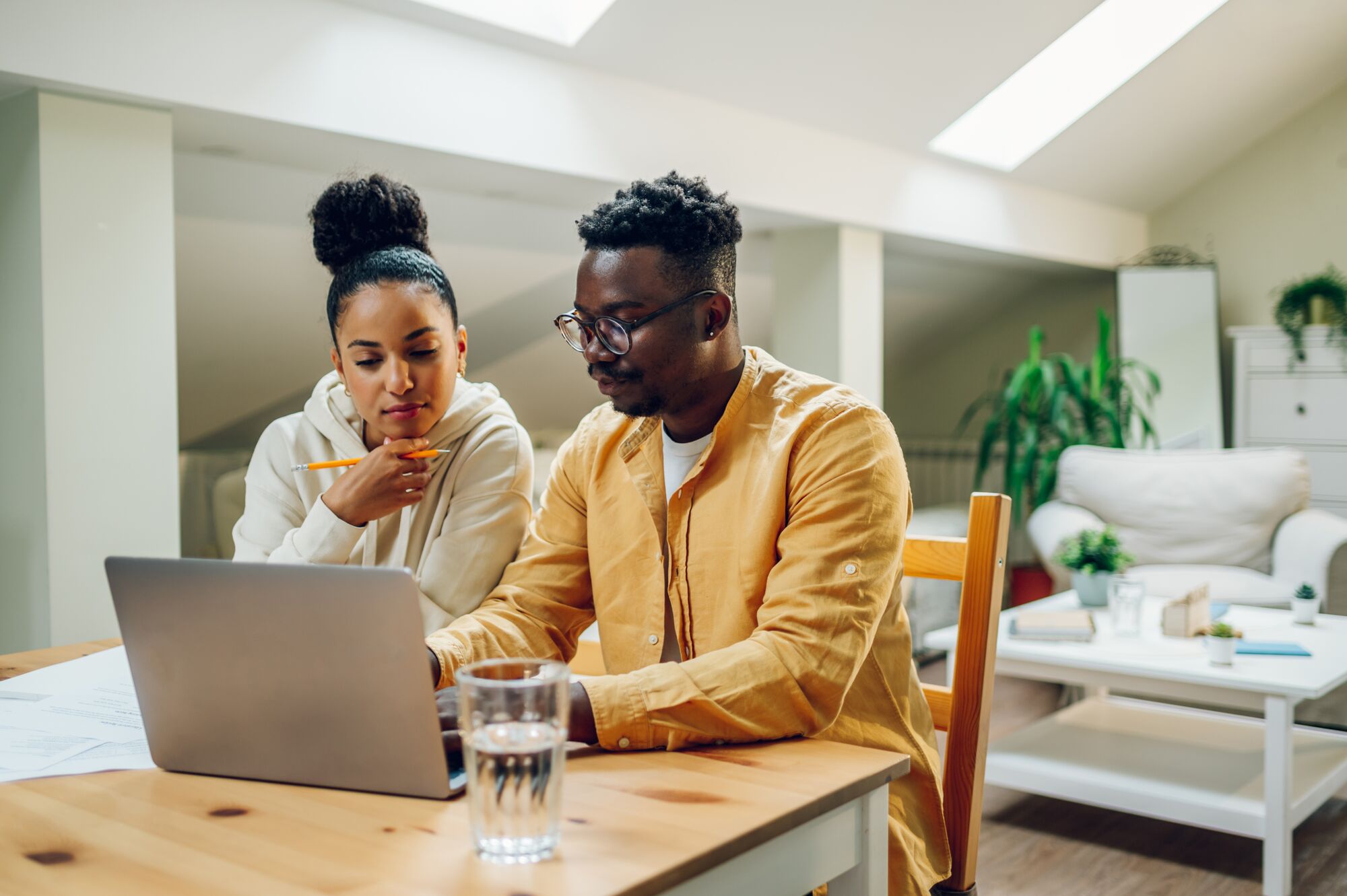 Diverse couple looking into laptop and planning their future while making a financial plan. Online banking, paying rant and bills. Both looking into the computer screen.
