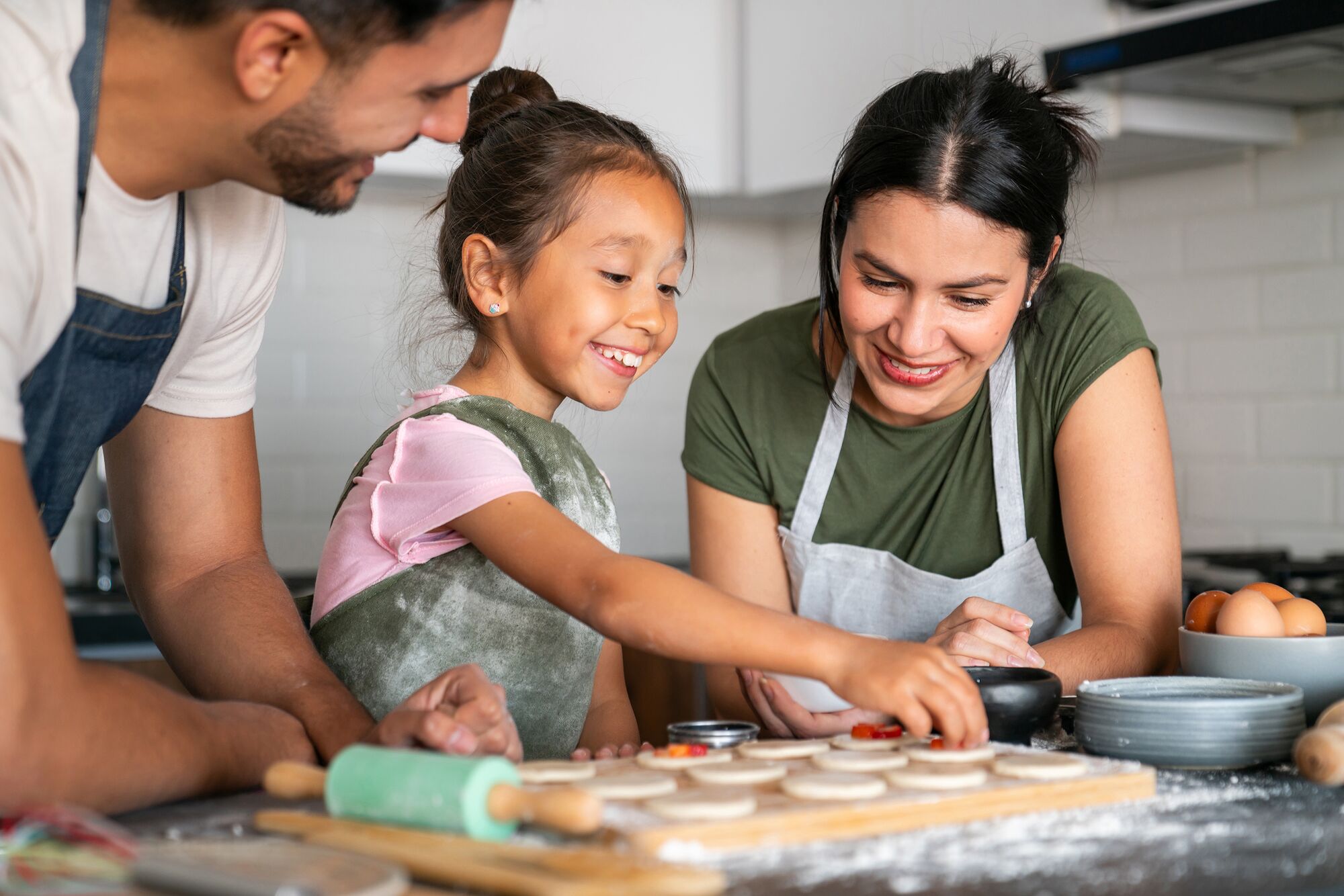 Happy Latin American girl baking at home with her loving parents - family lifestyle concepts