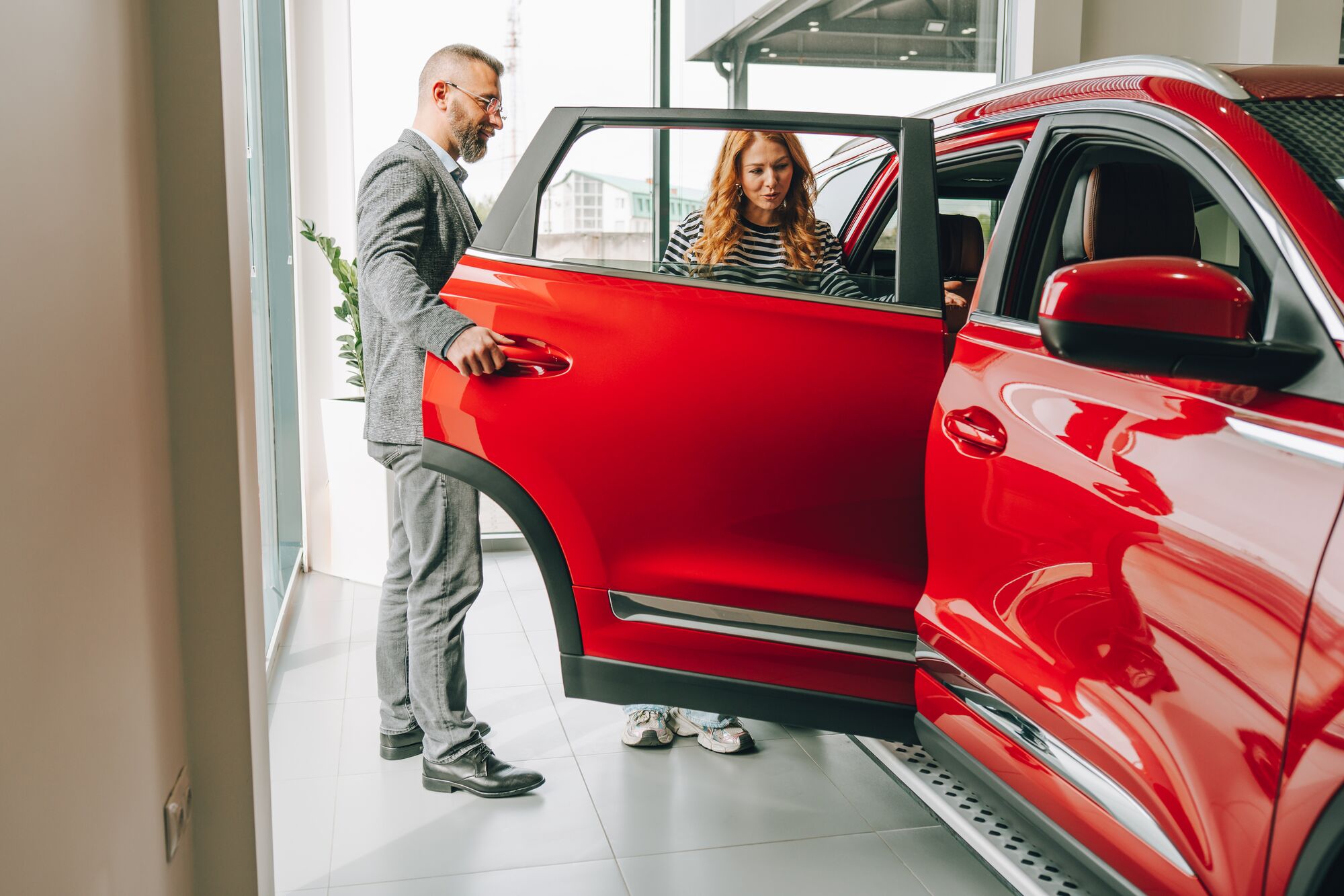 Salesman showing a new red car to a customer in a car dealership