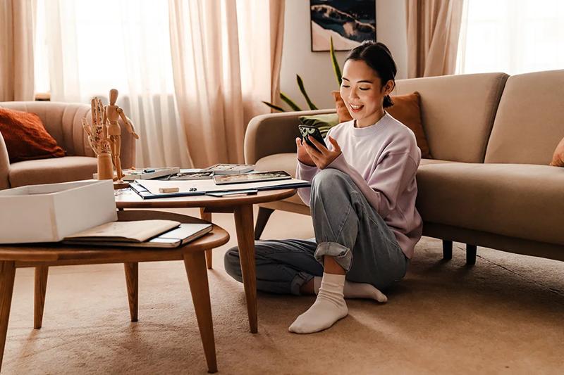 Woman using a smartphone while sitting on the floor beside a coffee table in her living room.
