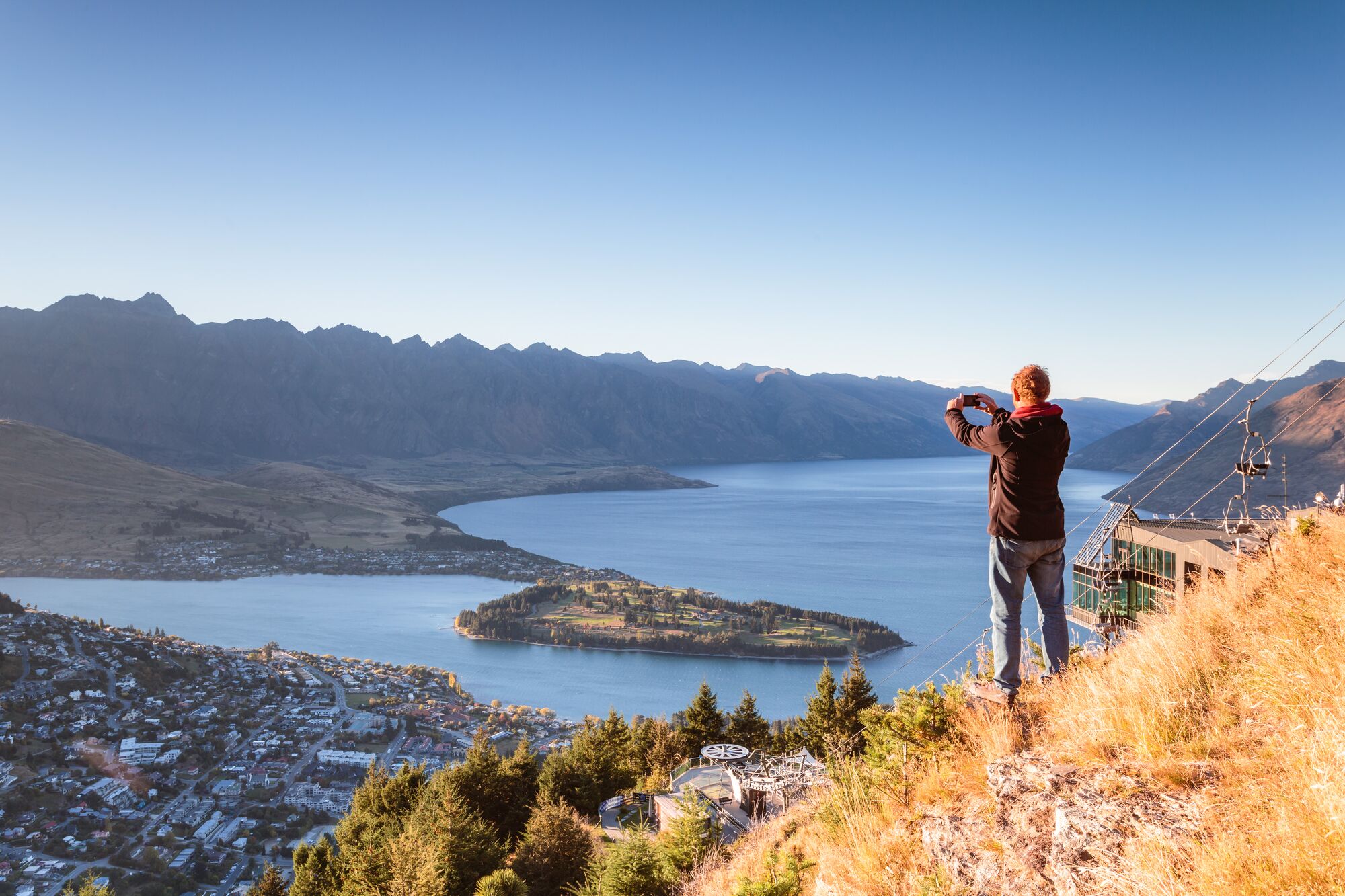 Hiker looking at Queenstown from lookout at sunrise, Otago, New Zealand