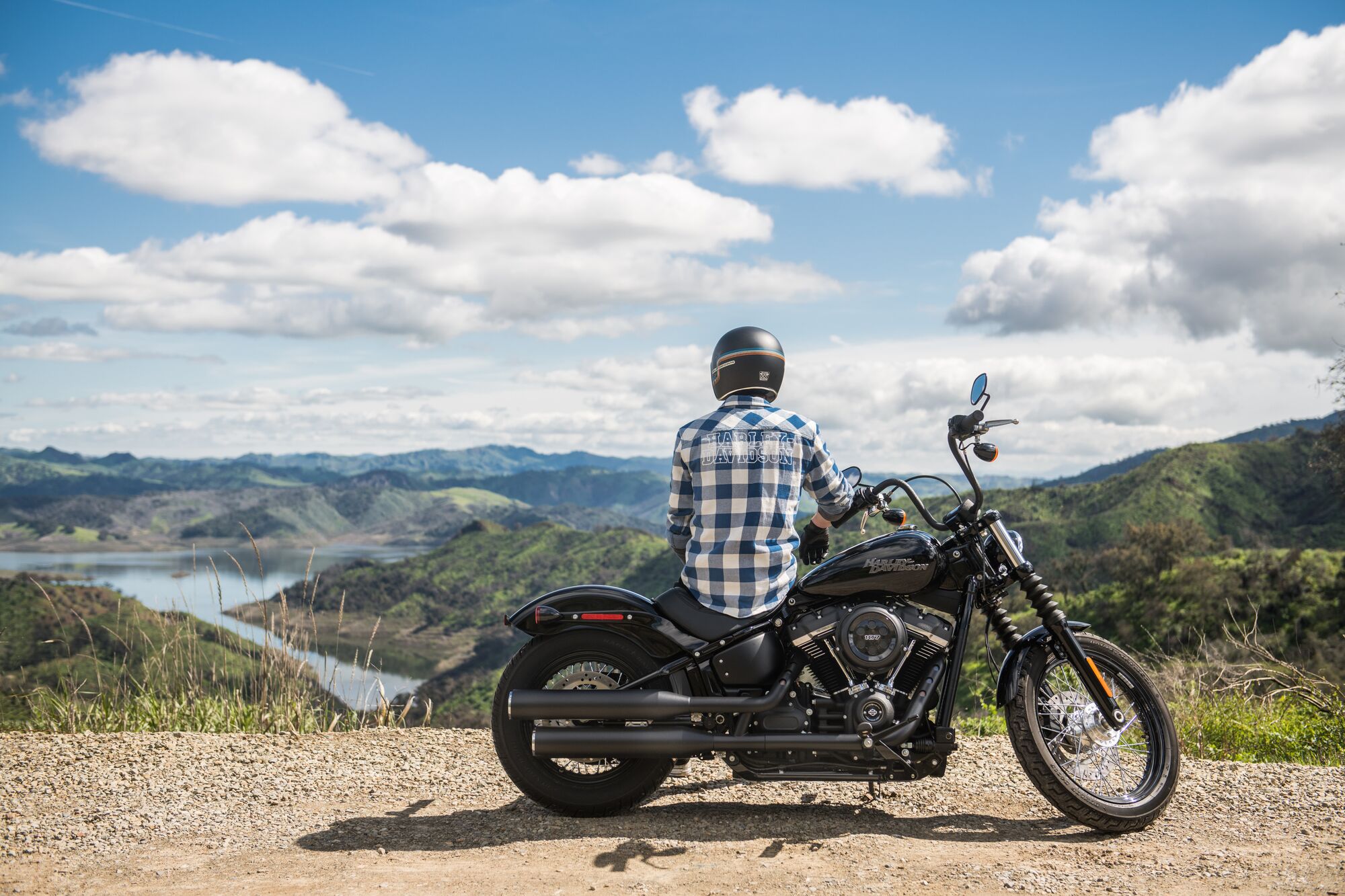 Motorcycle and rider sitting on side of road overlooking a river and forest