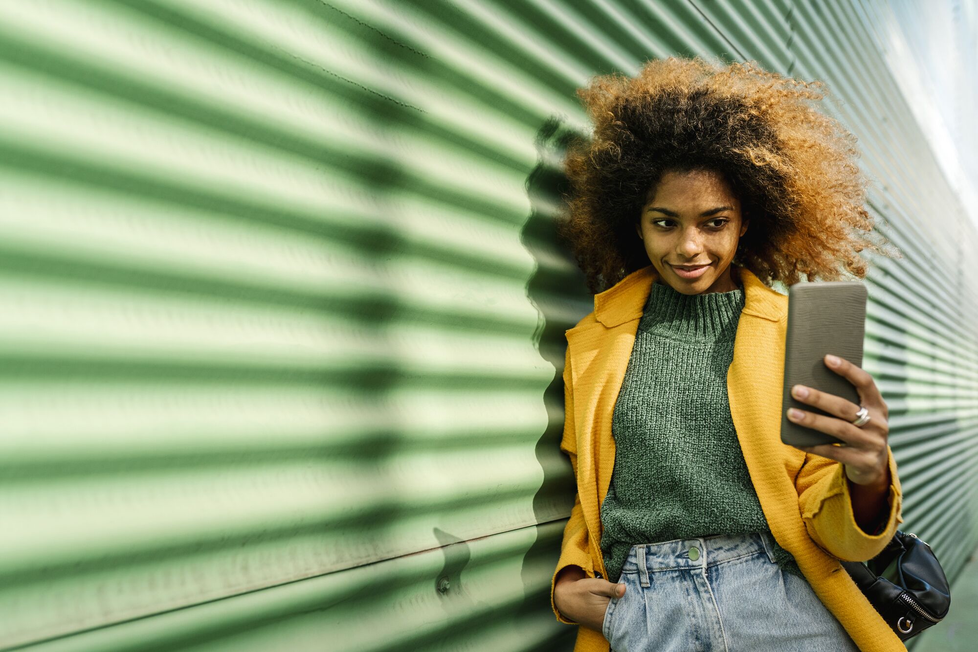 Valencia, Spain. Young woman with afro hair, using the phone on a green background.