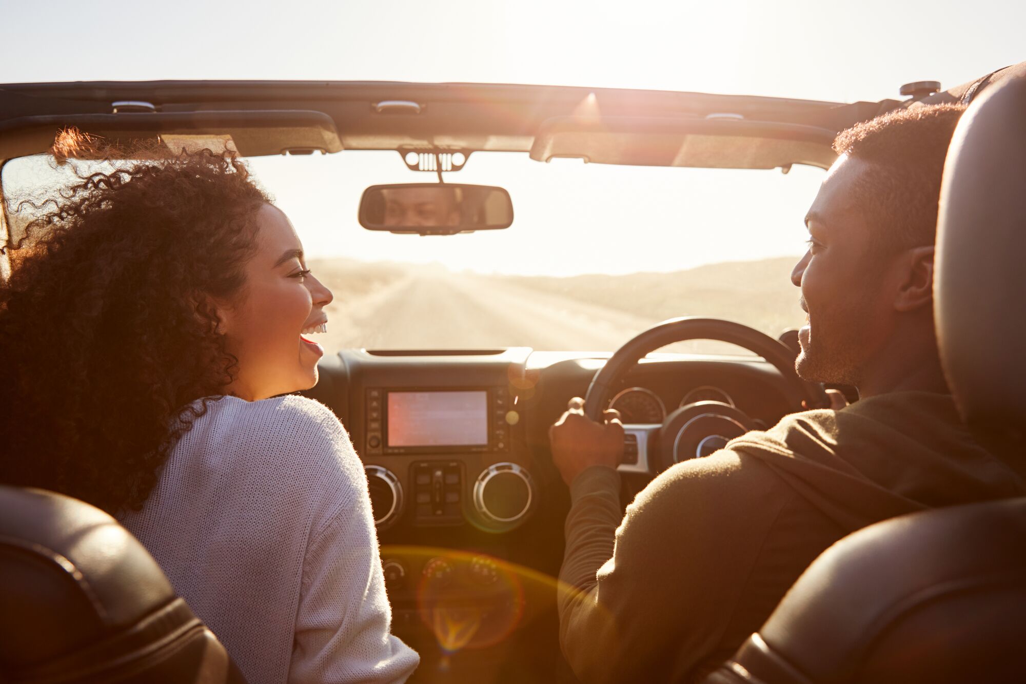 Happy couple drive looking at each other, rear passenger POV