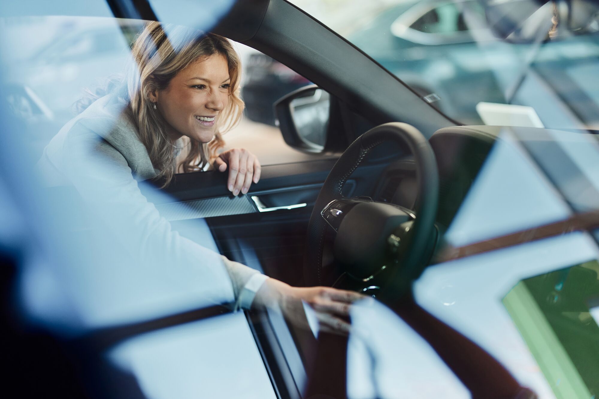 Happy woman looking at car interior while shopping in a showroom. The view is through glass.