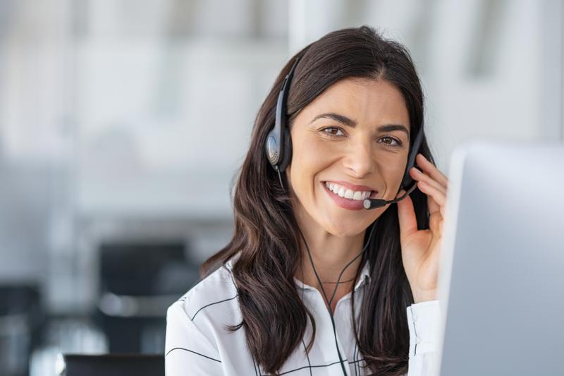 Call center agent with headset working on support hotline in modern office with copy space. Portrait of mature positive agent in conversation with customer over headset looking at camera.