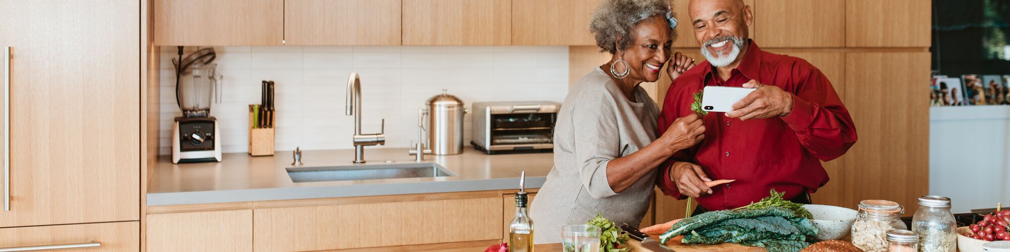Smiling senior couple watching video while preparing vegan meal in kitchen. Retired man and woman are standing with vegetable at kitchen island. They are spending leisure time at home.