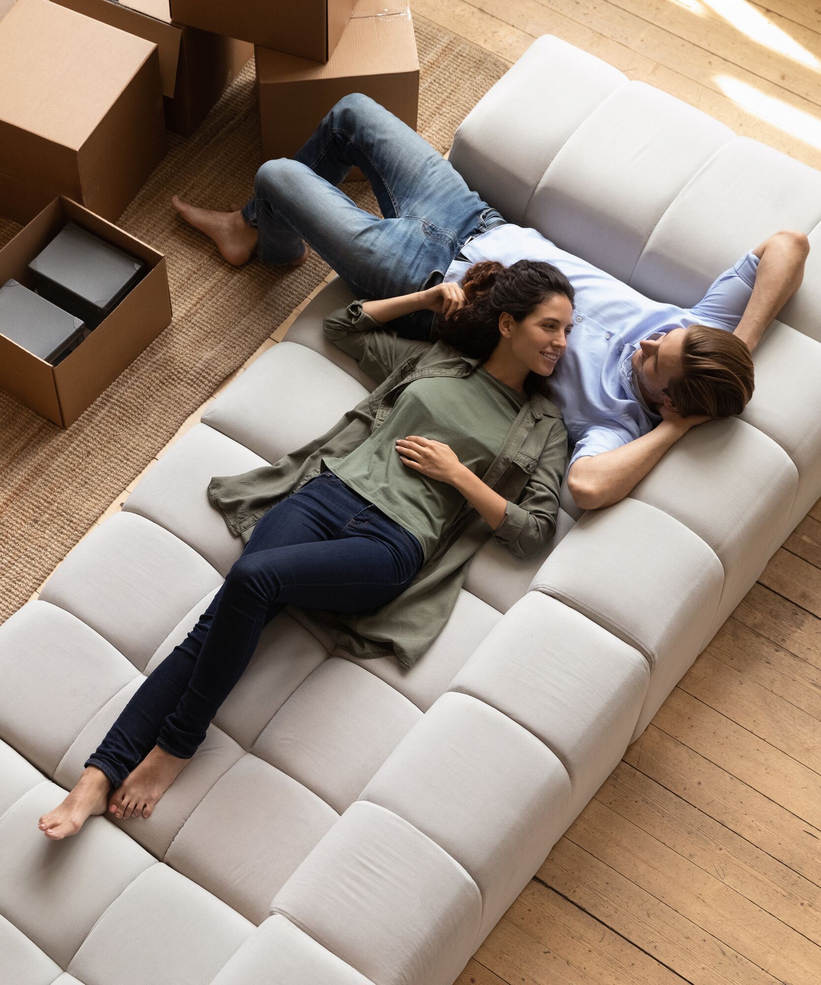 Overhead view peaceful young couple relaxing on fashionable cozy sofa near heap of packed belongings in cardboard boxes, resting at own house at relocation day. Bank loan and mortgage, tenancy concept
