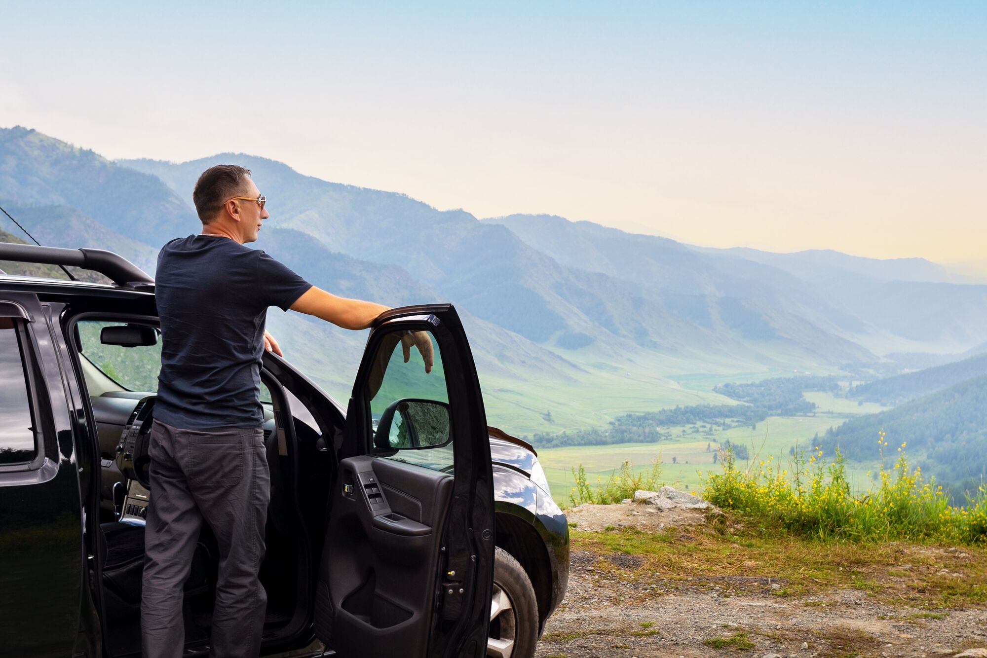 Man traveler standing near car with mountain background in evening time at sunset.