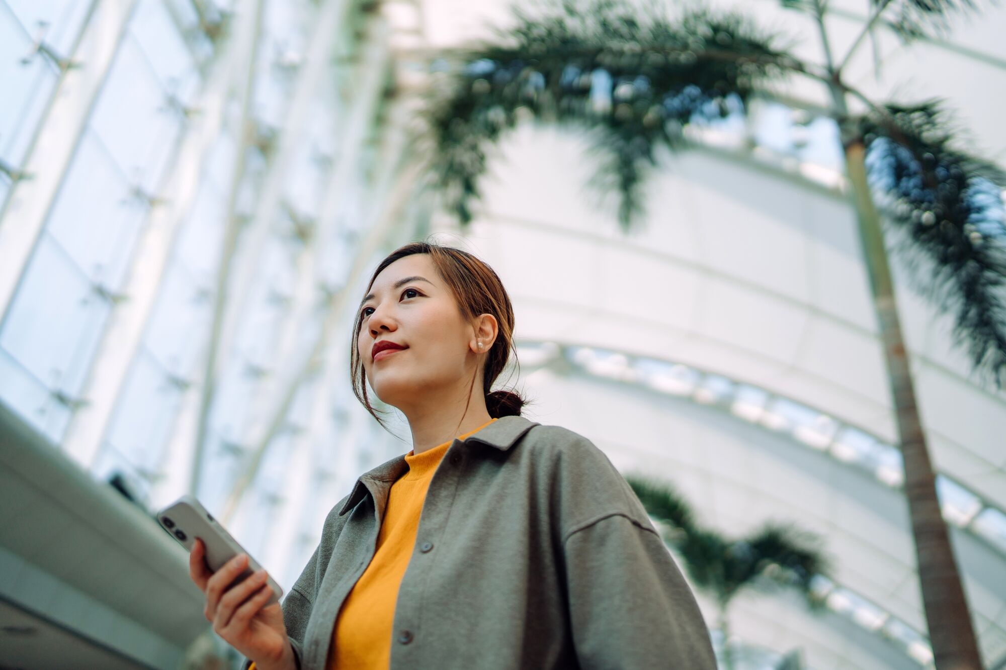 Professional young Asian businesswoman using smartphone in modern green office.