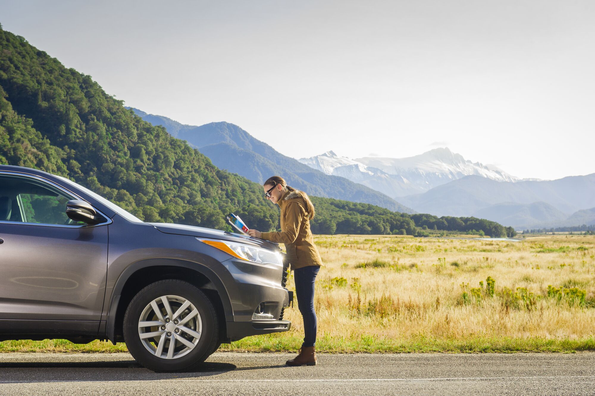 Hispanic woman wearing coat reading map on car hood