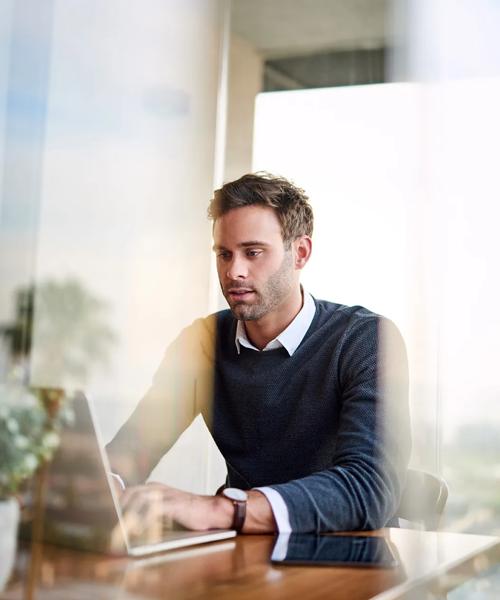 Focused young businessman working online with a laptop while sitting at a table at home