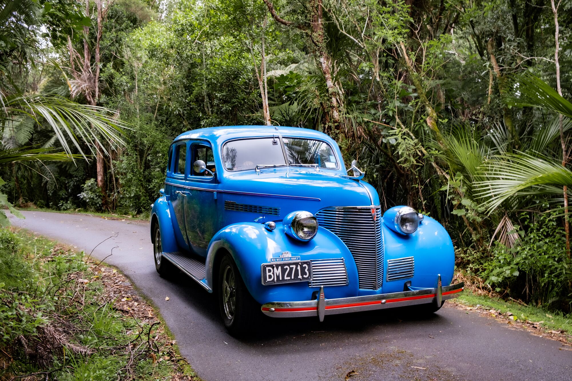 wide shot of blue classic car on a wooded path
