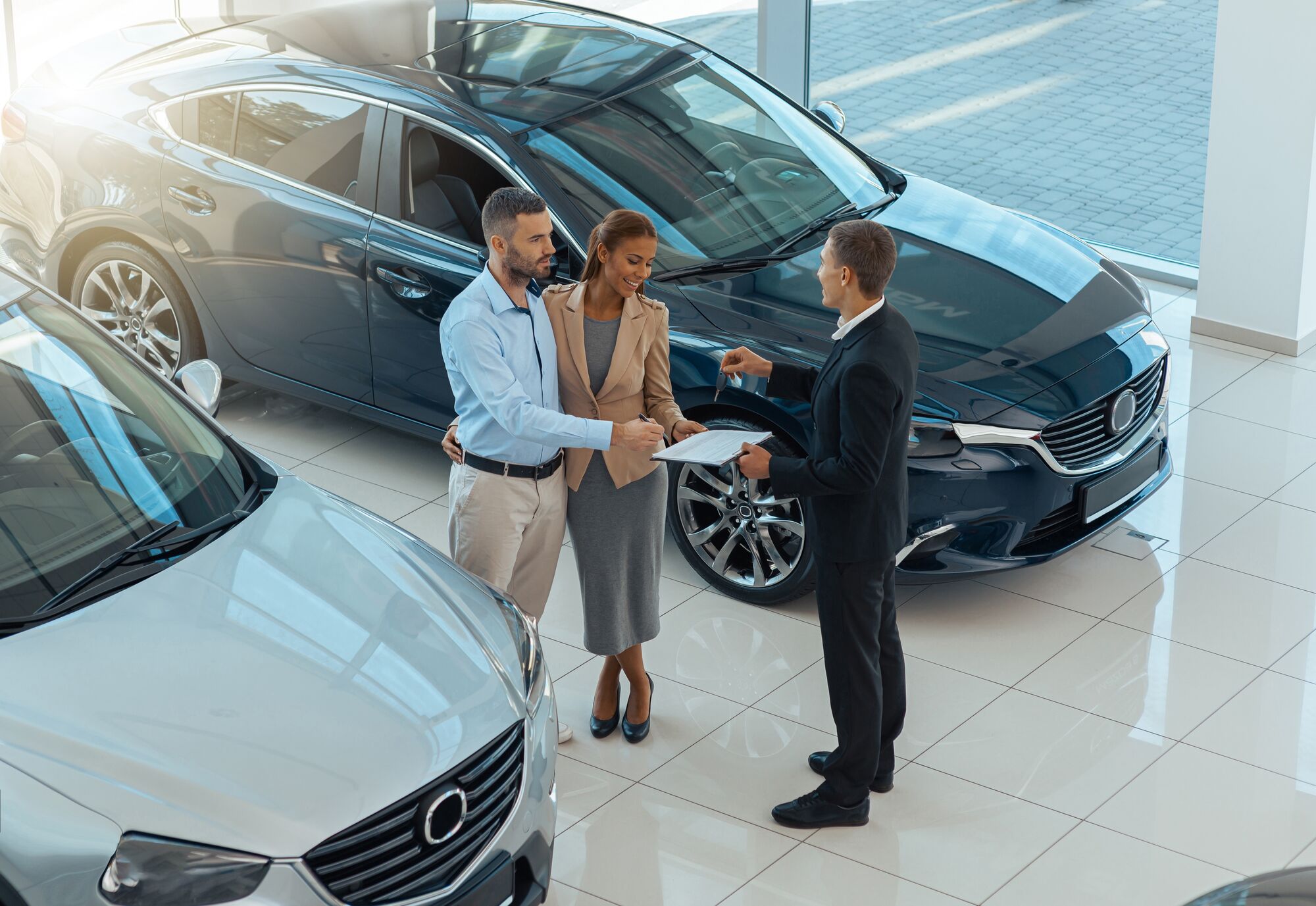 Happy beautiful couple is choosing a new car at dealership. Blurred background