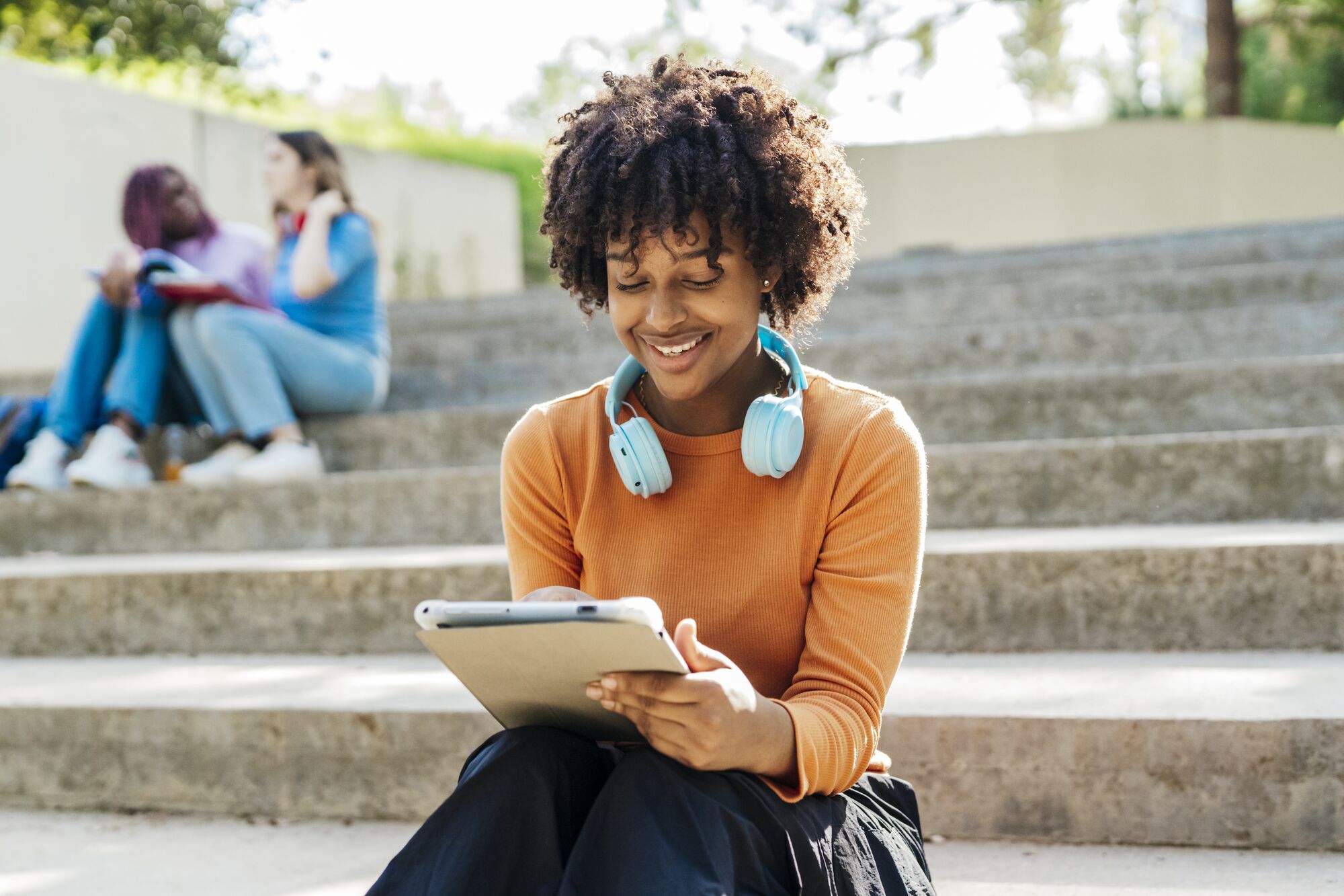 CL-DEVICES-YoungLadyHeadphonesTabletOutdoorSteps-GettyImages-1439357046